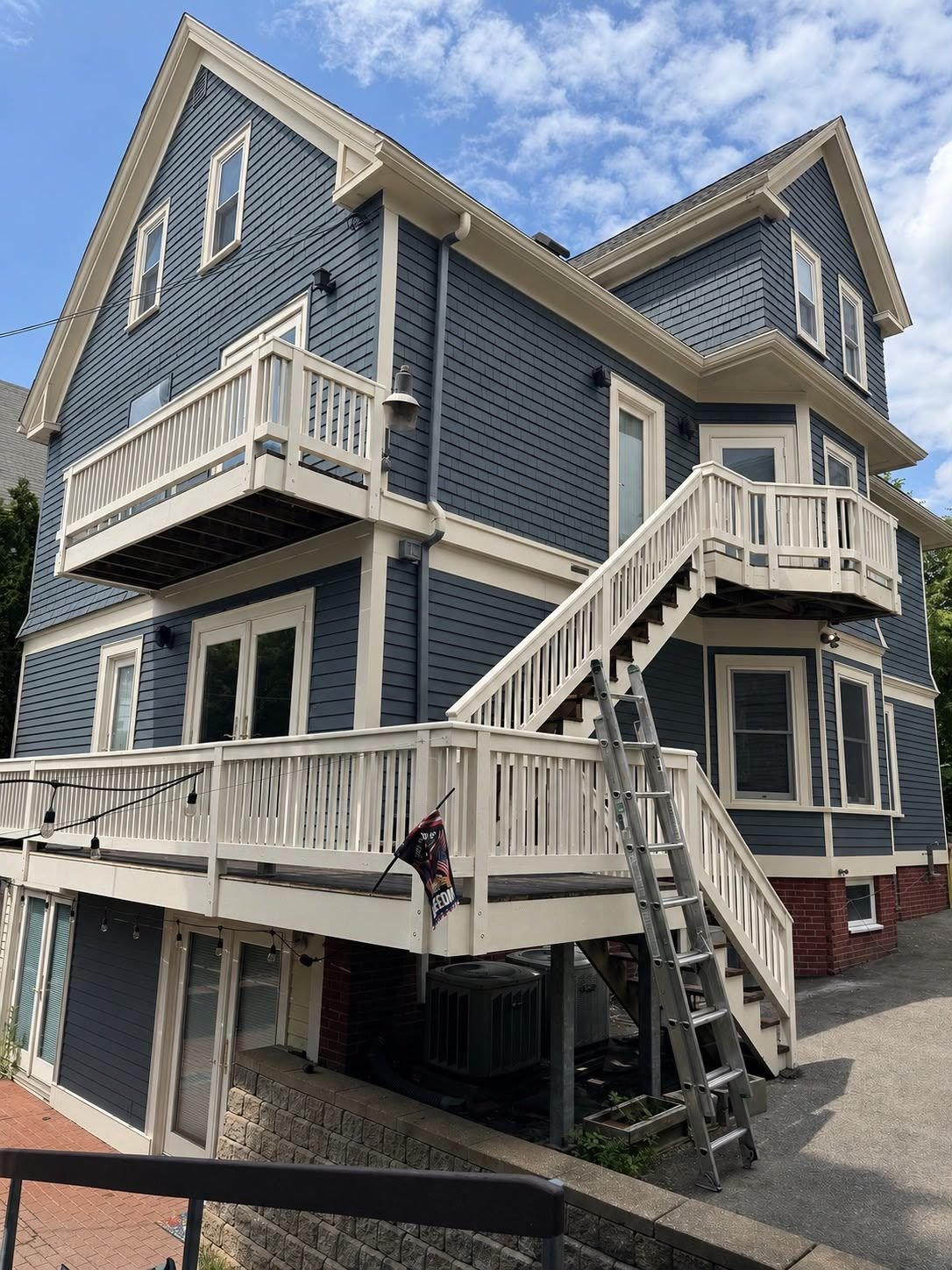 Three-story multi-family house with slate blue siding and off-white trim and porches after exterior painting